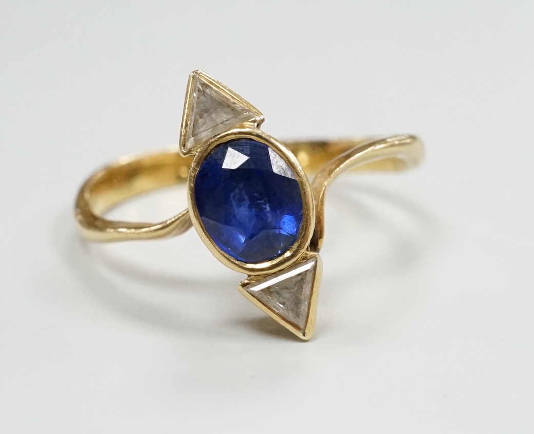 A yellow metal and single stone oval cut sapphire and two stone triangular cut diamond set ring, size L/M, gross weight 2.4 grams.